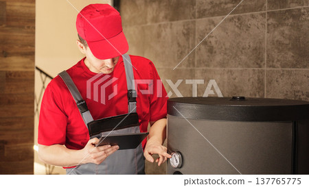 Technician inspecting boiler system and checking equipment with tablet during heating maintenance service and safety inspection. Technician inspecting boiler system and checking equipment with tablet during heating maintenance service and safety inspection. 137765775