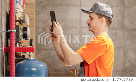 Professional Plumber Or HVAC Technician Inspecting Residential Boiler Heating System Using Digital Tablet During Technical Maintenance Service In Boiler Room 137765789