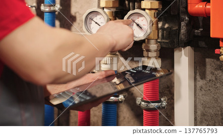 Technician Checking Heating System Gauges And Monitoring Boiler Data Using Digital Tablet In Utility Room. Residential HVAC Inspection And Plumbing Maintenance Diagnostics Concept. 137765793