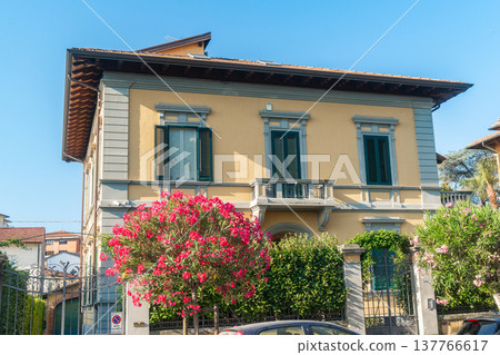 Italian house facade decorated with blooming pink flowers and green shutters. Bright summer day and Mediterranean lifestyle atmosphere. Italian house facade decorated with blooming pink flowers and green shutters. Bright summer day and Mediterranean lifestyle atmosphere. 137766617