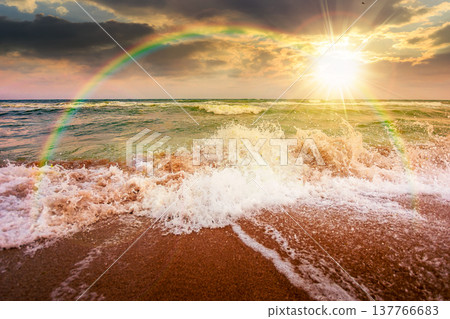 stormy weather on the sandy beach at sunset. dramatic sky over the sea in evening light. moody summer landscape. green waves crashing the shore. majestic cloudscape and rainbow above the horizon stormy weather on the sandy beach at sunset. dramatic sky over the sea in evening light. moody summer landscape. green waves crashing the shore. majestic cloudscape and rainbow above the horizon 137766683