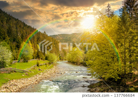 sunset over river in mountain landscape. wonderful springtime countryside scenery. blue green water among forest and rocky shore. wooden fence on the river bank. cloudy sky and rainbow 137766684
