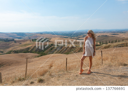 Woman walking along a rural path with panoramic countryside views. Summer travel, freedom, slow life and scenic landscape concept Woman walking along a rural path with panoramic countryside views. Summer travel, freedom, slow life and scenic landscape concept 137766691