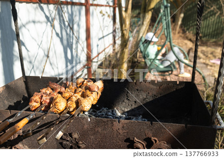 Grilling meat skewers over charcoal in sunny backyard 137766933