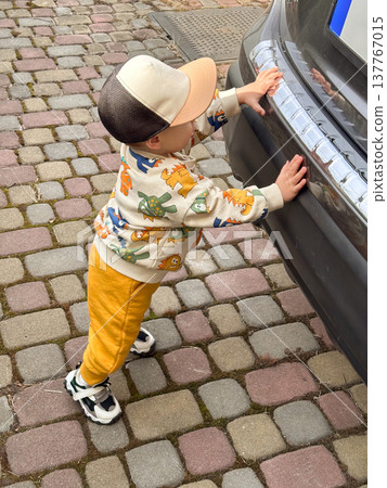 Toddler standing beside car on cobblestone driveway Toddler standing beside car on cobblestone driveway 137767015