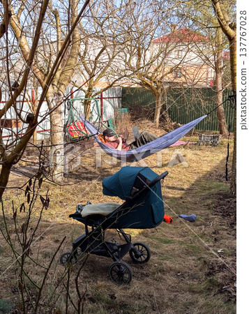 Person relaxing in hammock in backyard with stroller Person relaxing in hammock in backyard with stroller 137767028