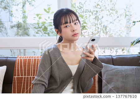 A woman thinking with her smartphone in hand; a relaxed lifestyle in the living room. A woman thinking with her smartphone in hand; a relaxed lifestyle in the living room. 137767610