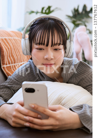 A woman enjoying her smartphone with headphones on; a relaxed lifestyle in the living room. A woman enjoying her smartphone with headphones on; a relaxed lifestyle in the living room. 137767612