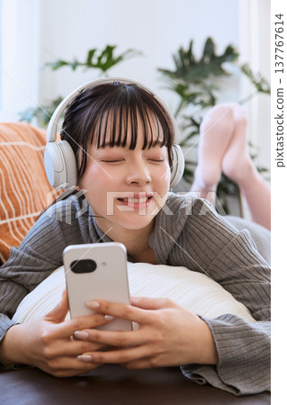 一位女士戴著耳機欣賞音樂;用智慧型手機放鬆休閒。 一位女士戴著耳機欣賞音樂;用智慧型手機放鬆休閒。 137767614