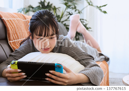 A woman playing a handheld game console; relaxing at home on a holiday. 137767615
