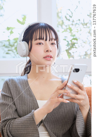 一位女士戴著耳機使用智慧型手機:一種居家生活方式 一位女士戴著耳機使用智慧型手機:一種居家生活方式 137767619