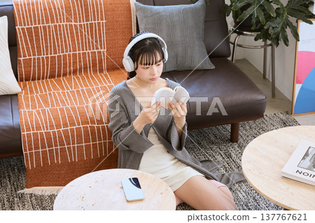 一位女士戴著耳機聽音樂，在家放鬆看書。 137767621