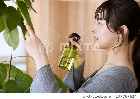 一位年輕女子用噴霧瓶為盆栽植物澆水。 一位年輕女子用噴霧瓶為盆栽植物澆水。 137767624