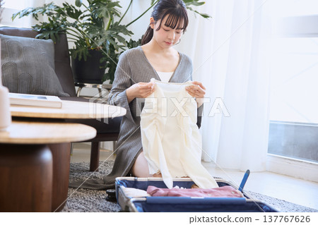 A young woman packs clothes into a suitcase in preparation for a trip. A young woman packs clothes into a suitcase in preparation for a trip. 137767626