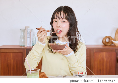 A young woman eating an acai bowl for breakfast. 137767637