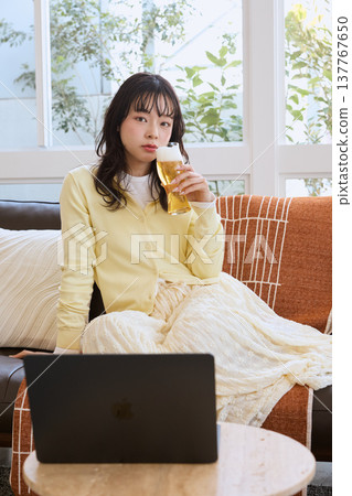 一位女士在家一邊喝啤酒一邊看影片。 一位女士在家一邊喝啤酒一邊看影片。 137767650