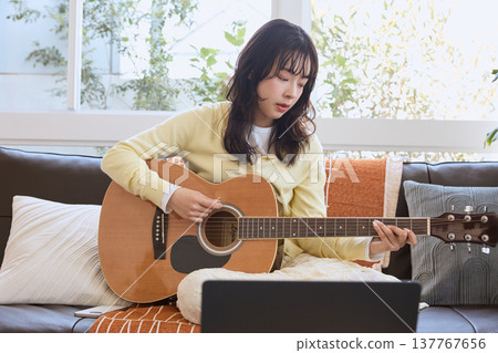A woman practicing guitar online 137767656