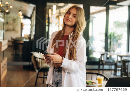 Standing and holding smartphone. Young woman is in the cafe at daytime 137767669