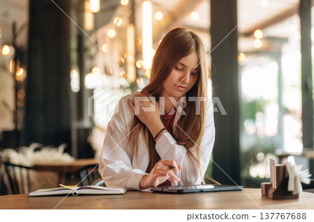 Using digital tablet, sitting, front view. Young woman is in the cafe at daytime Using digital tablet, sitting, front view. Young woman is in the cafe at daytime 137767688
