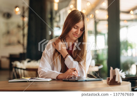 Using digital tablet, sitting, front view. Young woman is in the cafe at daytime Using digital tablet, sitting, front view. Young woman is in the cafe at daytime 137767689