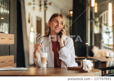 Conversation by phone, talking. Young woman is in the cafe at daytime Conversation by phone, talking. Young woman is in the cafe at daytime 137767691