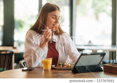 Using digital tablet, sitting, front view. Young woman is in the cafe at daytime Using digital tablet, sitting, front view. Young woman is in the cafe at daytime 137767693