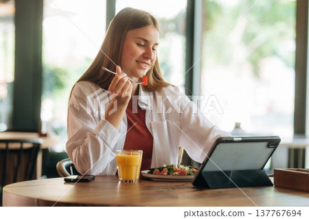 Using digital tablet, sitting, front view. Young woman is in the cafe at daytime Using digital tablet, sitting, front view. Young woman is in the cafe at daytime 137767694