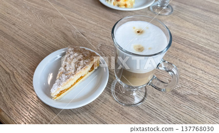 Slice of fruit crumble cake with powdered sugar served with layered latte macchiato in a cozy cafe Slice of fruit crumble cake with powdered sugar served with layered latte macchiato in a cozy cafe 137768030