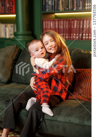 Child holds baby on green couch in cozy indoor setting during daytime Child holds baby on green couch in cozy indoor setting during daytime 137768506