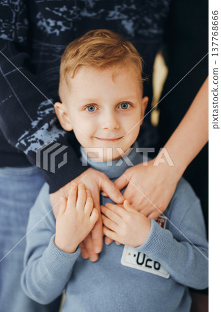 A young boy with blue eyes smiles while standing between his parents A young boy with blue eyes smiles while standing between his parents 137768666