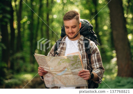 Searching the way, holding map. Male tourist is with backpack in the forest Searching the way, holding map. Male tourist is with backpack in the forest 137768821