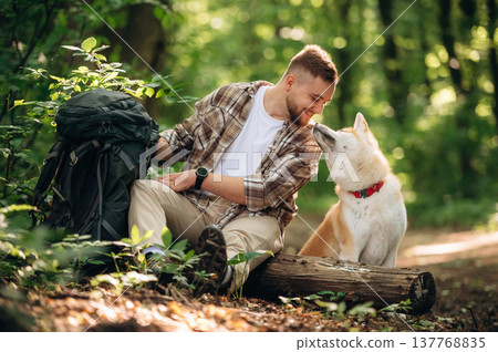 Tranquil, resting by sitting on the log. Man tourist is with his dog in the forest 137768835