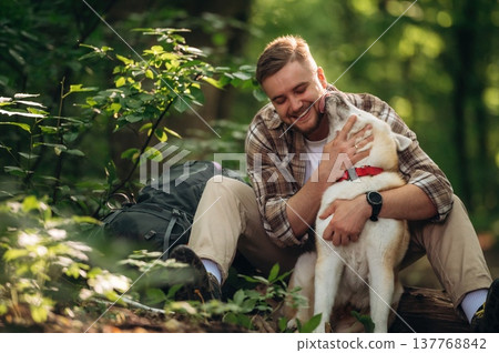 Owner of the pet is happy, playing with him. Man tourist is with his dog in the forest Owner of the pet is happy, playing with him. Man tourist is with his dog in the forest 137768842