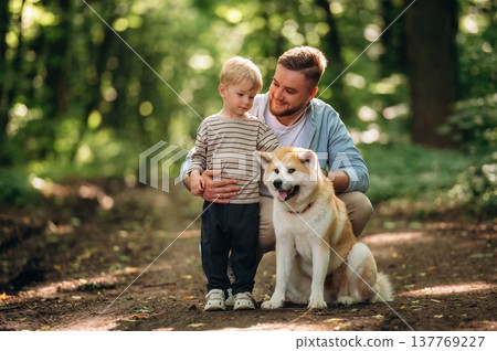 Sitting, playing with pet. Father with son and dog are in the forest Sitting, playing with pet. Father with son and dog are in the forest 137769227