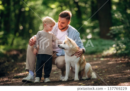 Cheerful, sitting and smiling. Father with son and dog are in the forest 137769229