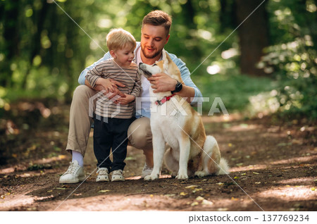 Positive facial expression, sitting. Father with son and dog are in the forest Positive facial expression, sitting. Father with son and dog are in the forest 137769234