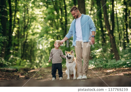 Front view, having a walk. Father with son and dog are in the forest Front view, having a walk. Father with son and dog are in the forest 137769239