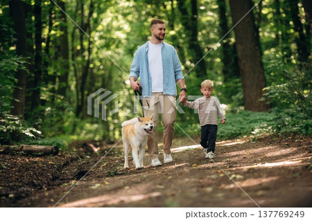 Free time, having a walk, wellness. Father with son and dog are in the forest Free time, having a walk, wellness. Father with son and dog are in the forest 137769249