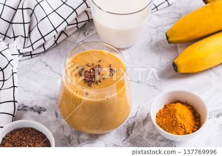 Mix of banana, turmeric and plant milk in a glass on a table 137769996