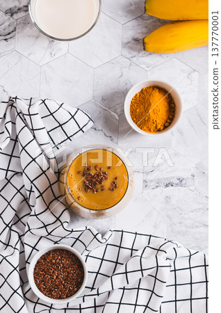 Mix of banana, turmeric and plant milk in a glass on a table top and vertical view Mix of banana, turmeric and plant milk in a glass on a table top and vertical view 137770001