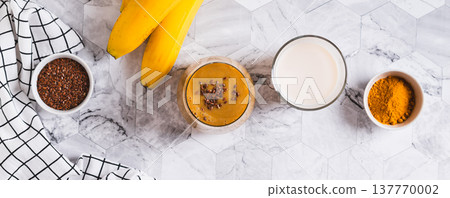 Mix of banana, turmeric and plant milk in a glass on a table top view web banner Mix of banana, turmeric and plant milk in a glass on a table top view web banner 137770002