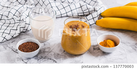 Smoothie made from coconut milk, banana, turmeric and flax seeds in a glass web banner Smoothie made from coconut milk, banana, turmeric and flax seeds in a glass web banner 137770003