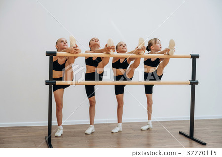 Stretching the legs. Girls practicing ballet indoors in the class Stretching the legs. Girls practicing ballet indoors in the class 137770115