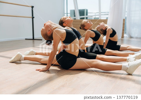 Stretching the legs. Girls practicing ballet indoors in the class 137770119