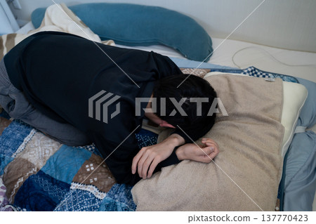 A man sleeping with his face buried in the pillow under his futon. A man sleeping with his face buried in the pillow under his futon. 137770423