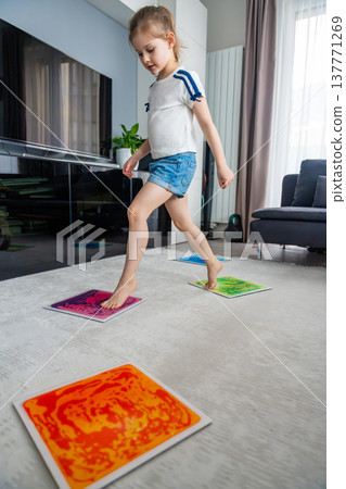 Little girl stepping and jumping on colorful sensory gel mats placed on floor at home. Sensory development, autism support and occupational therapy activity concept. Little girl stepping and jumping on colorful sensory gel mats placed on floor at home. Sensory development, autism support and occupational therapy activity concept. 137771269