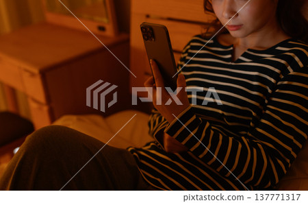 一名女子在黑暗的房間裡操作智慧型手機。 一名女子在黑暗的房間裡操作智慧型手機。 137771317