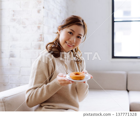 一位微笑的日本女性手拿甜甜圈。 137771328