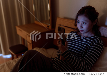 一名婦女在床上的看一個智能手機 137771344