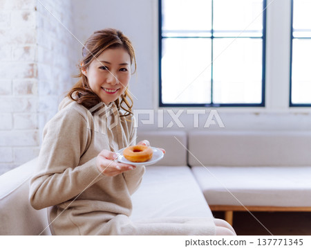 一位女士在家中放鬆地享用甜甜圈。 137771345